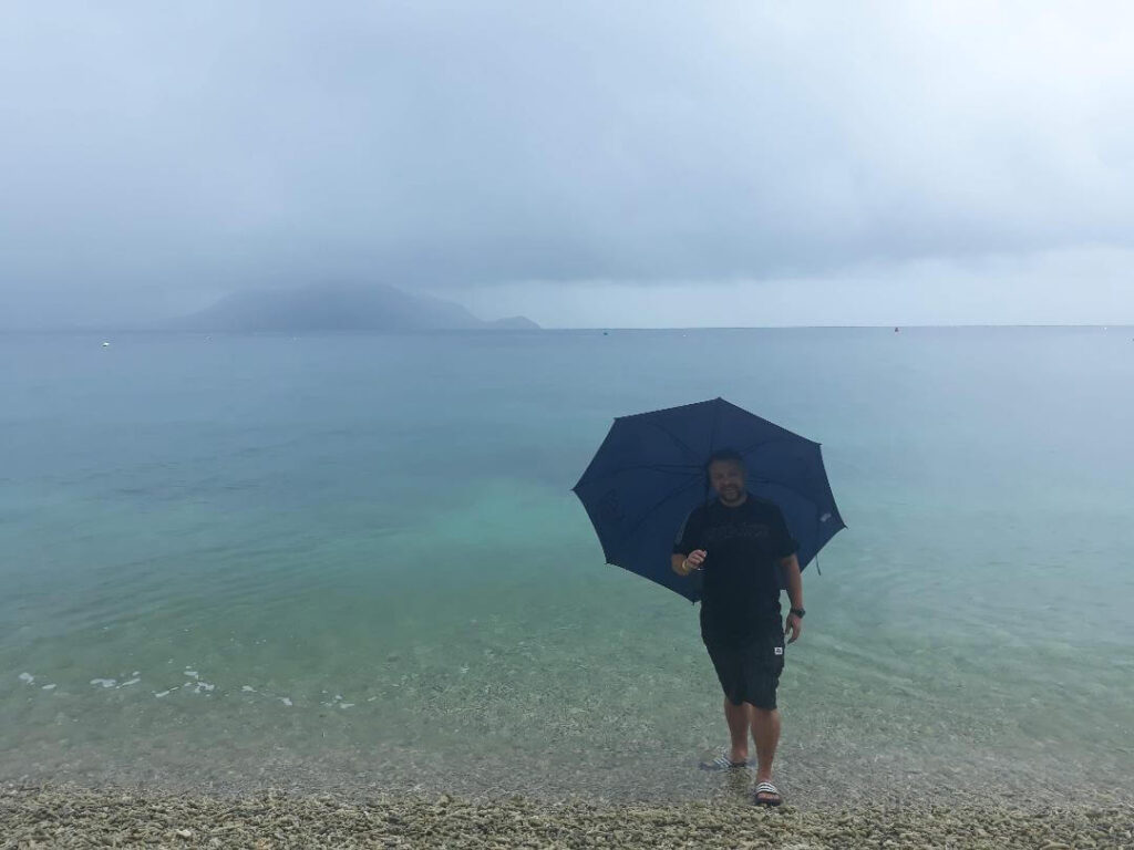 Kevin on a beach with an umbrella in the rain Is Cairns Worth Visiting? The Best Guide Out There Happy Irish Wanderers